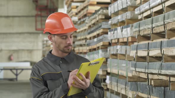 Handsome Male Warehouse Worker Walking Writing on His Clipboard