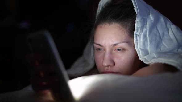 girl at night uses the phone, lying under the covers