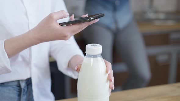 Closeup of Unrecognizable Woman Scanning QR Code on Milk Bottle with Smartphone