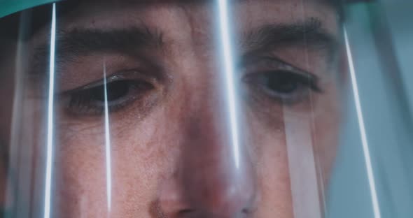 Researcher is viewed closeup in the workplace wearing protective face screen over his eyes