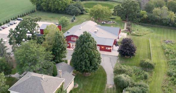 Big red barn is revealed from behind the green trees on a farm field in Wisconsin in summer.