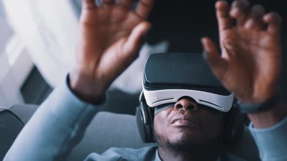 AfricanAmerican Man Wearing Virtual Reality Glasses and a Headset Touching Air with Hands