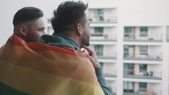 Young Homosexual Couple Enjoying the View From the Balcony Covered with Pride Rainbow Flag