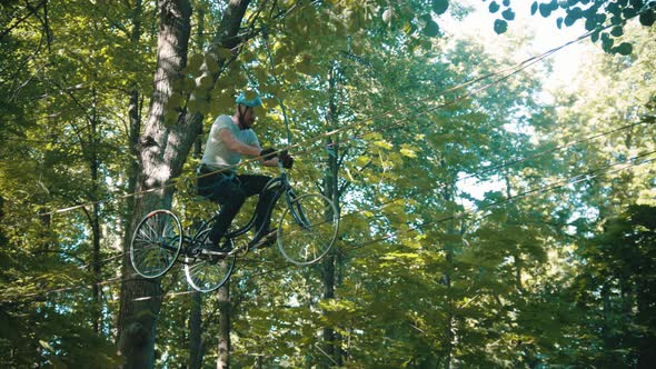 A Man Crossing the Ropes Between Two Trees on the Bicycle