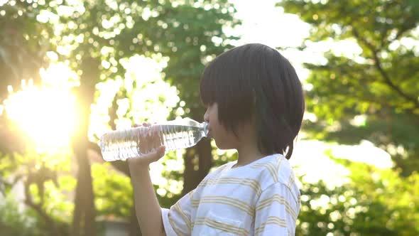 Cute Asian Boy Drinking Water From A Bottle In The Park