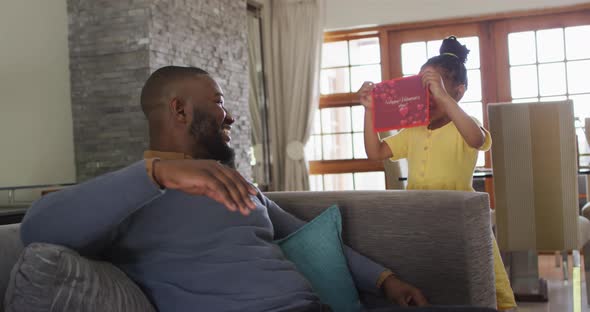 Happy african american daughter giving present to surprised father