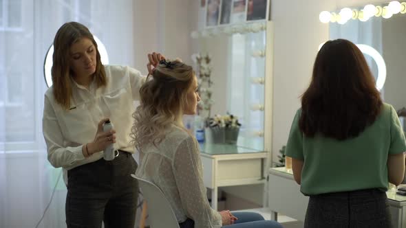 Hairdresser spraying the hairspray on hair of woman sitting in front of mirror.