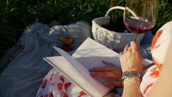 Young Woman Enjoying Picnic In Park With Book Drinking Wine.