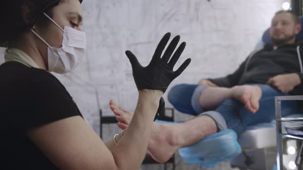 Man Having Pedicure Procedure  Master Putting Black Glove