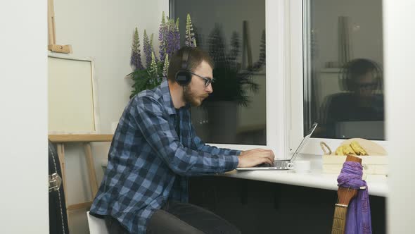 Young man IT programmer in headphones listening to music and typing on laptop computer keyboard