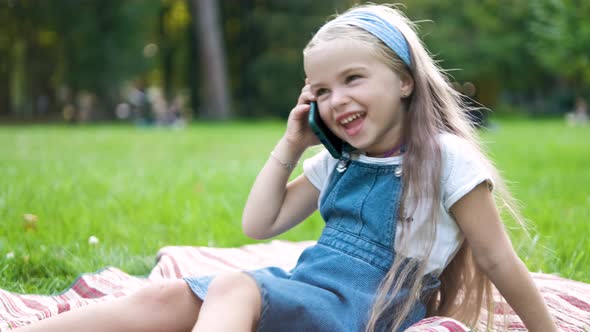 Happy Little Child Girl Having Conversation Talking on Her Sellphone in Summer Park