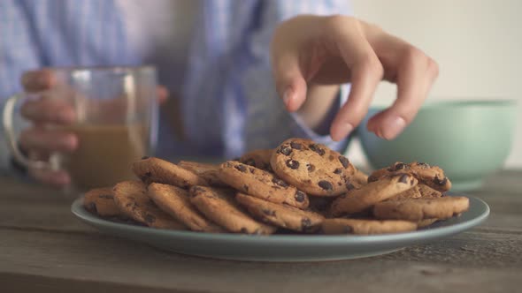 The Girl Drinks Coffee And Eats Cookies. Lots Of Chocolate Chip Cookies On A Gray Plate.