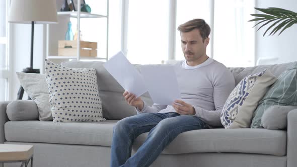 Pensive Adult Man Reading Documents while Sitting on Couch