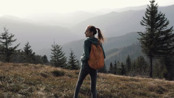 Happy Woman Hiker Walking on Edge of Mountain Ridge Against Background of Sunset