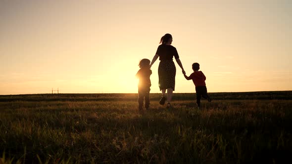 Silhouette of Young Family Mom and Two Brothers Twins Boys Runs to the Sun on Open Air Field or Park