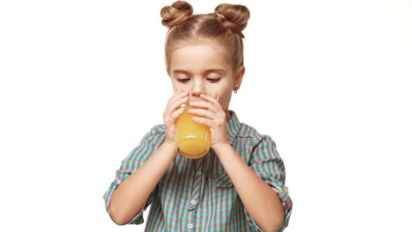 Cute Small Caucasian Girl Kid in Plaid Shirt and Hair Buns Drinking Orange Juice From Glass and