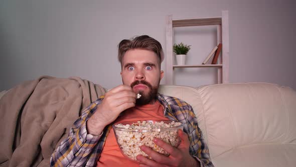 Home Cinema Concept. Shocked and Scared Man Watching Tv and Eating Popcorn