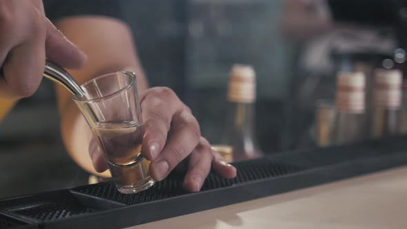 Section of Unrecognizable Bartender Pouring Alcohol Shots at Bar Counter to Little Glasses of Blue