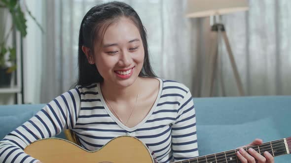 Close Up Of Asian Woman Having Video Call On Laptop And Playing A Guitar At Home
