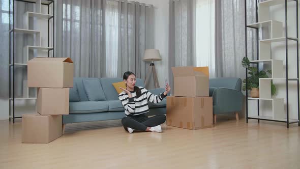 Young Asian Woman With Cardboard Boxes Live Stream By Smartphone After Moving Into A New House 