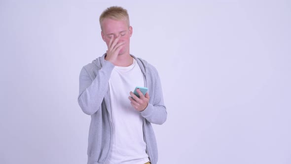 Stressed Young Blonde Man Using Phone and Getting Bad News
