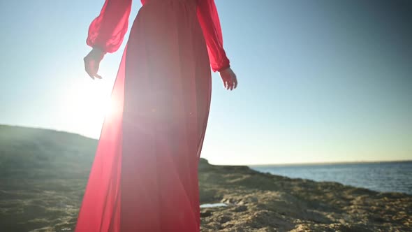 Slow Motion Young Caucasian Woman in a Loose Fluttering Red Dress is Walking Along the Rocky