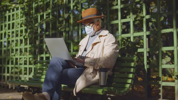Senior Businessman in Safety Mask Working on Computer Sitting in Bench in Park