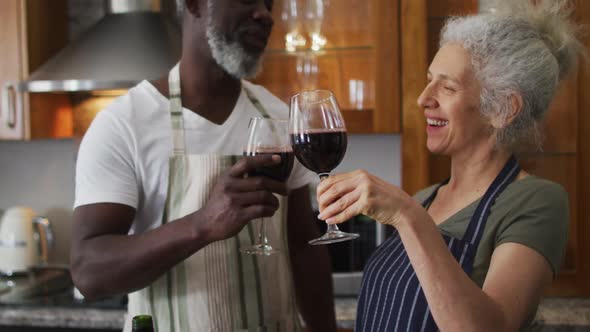 Mixed race senior couple toasting and drinking wine together in the kitchen at home