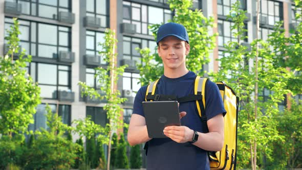 Smiling Delivery Man Courier with Thermal Bag Uses Tablet Confirm Client Order