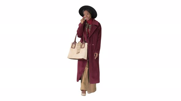 African American Fashion Girl in Coat and Black Hat Talking on the Phone While Walking on White