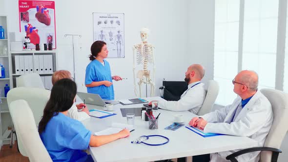 Assistent Pointing on Skeleton in Front of Medical Stuff