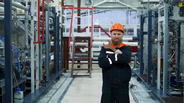 A Bearded Male Mechanic in an Orange Helmet with a Large Wrench Stands in a Fuel Gas Preparation