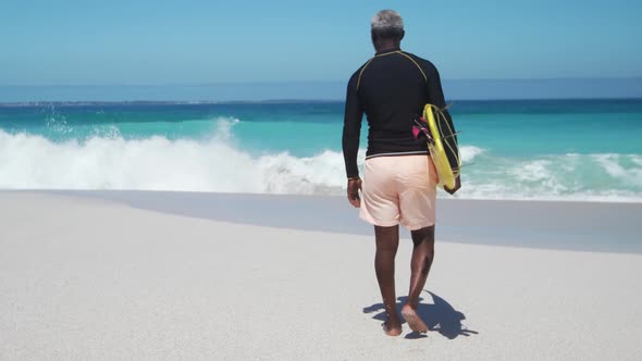 Senior man walking with surfboard at the beach