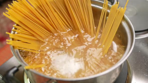 Raw spaghetti is being cooked in boiling water in a kitchen pot.