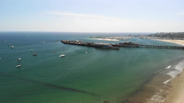 Aerial drone shot over the sandy beach with sail boats in the harbor and the dark blue Pacific Ocean