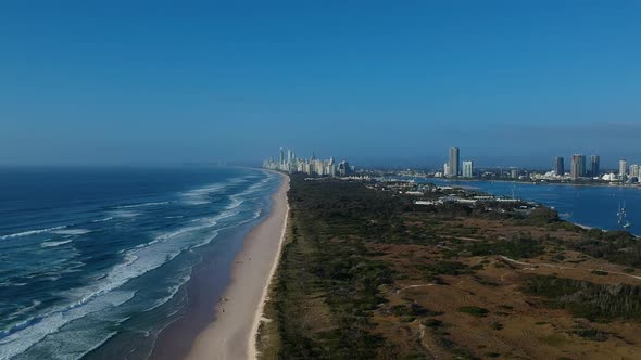 Aerial view of two bodies of water near a large area of green space with a city skyline in the dista