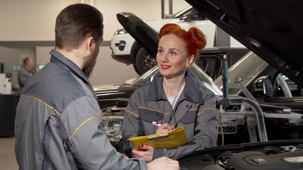 Lovely Female Mechanic Taking Notes, Talking To a Colleague at the Garage