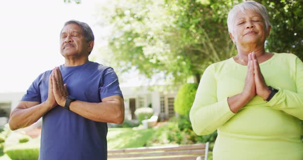 Video of relaxed biracial senior couple practicing yoga in garden