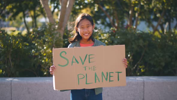 Portrait of Cute Teenage Asian Girl Holding Save the Planet Sign Protesting for Nature Outdoors
