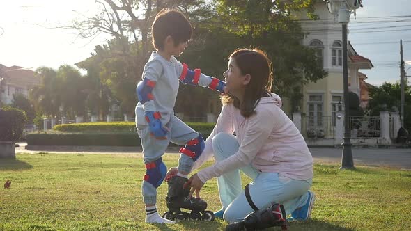 Asian Mother Helping Her Son Putting His Roller Skates On Enjoying Time Together In The Park