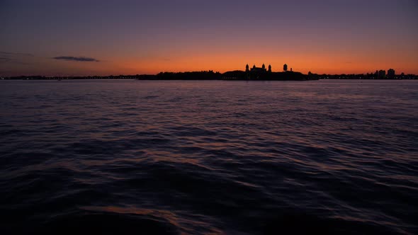 wide shot, from a boat, showing sailing ship, statue of liberty at dusk, teal and orange sky