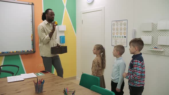 An African American Teacher and a Group of Children are Studying Fruits and Animals in the Classroom