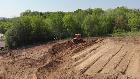 Aerial view of bulldozer flattening surface on further construction site