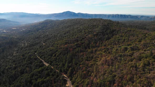 4K aerial shot of a highway winding through the mountains and forests of California.