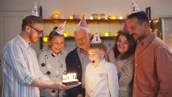 Happy Boy Celebrating Birthday with Family Blowing Out Candles on Cake