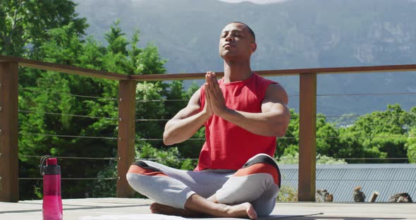 Relaxed biracial man sitting on terrace and meditating