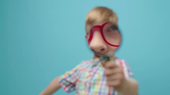 Preschool Boy Looking Through Magnifying Glass to the Camera Standing on Blue Background