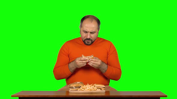 Funny Adult Man at a Table with a Plate of Fast Food Enjoys Eating a Burger and French Fries, Green