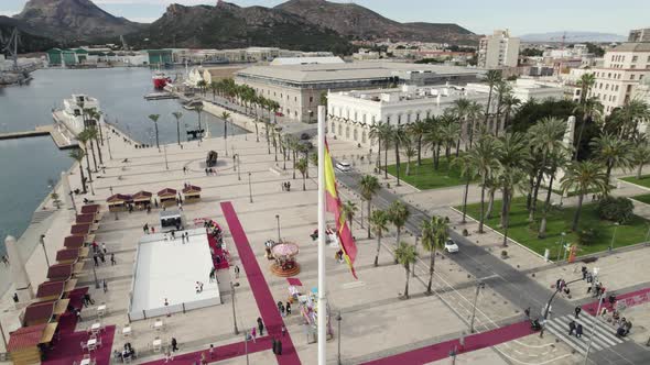 Aerial orbiting around Spanish flag on promenade of Cartagena touristic port, Spain