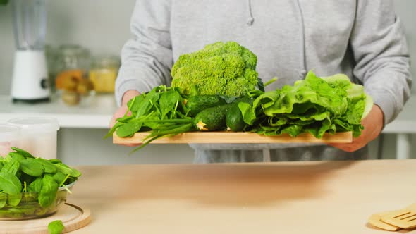 Putting Cutting Board with Fresh Greenery Vegetables on Table Closeup